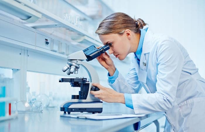 A clinical trial researcher looking at medical samples through her microscope in a research lab