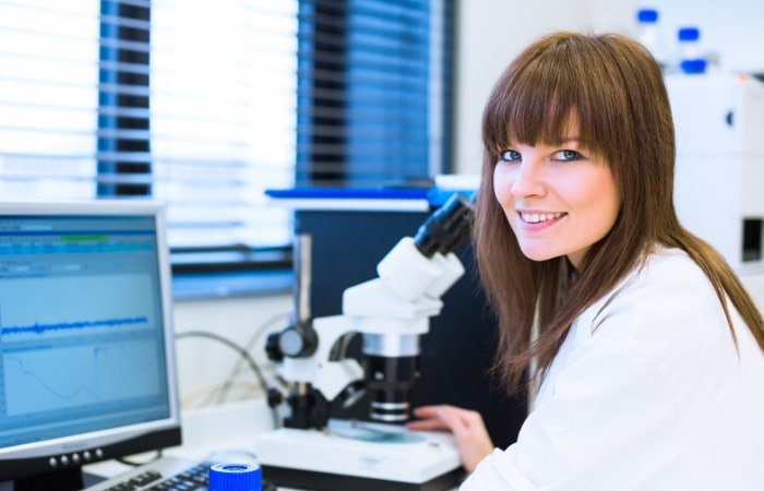 A woman doing medical research in front of a computer screen and a microscope