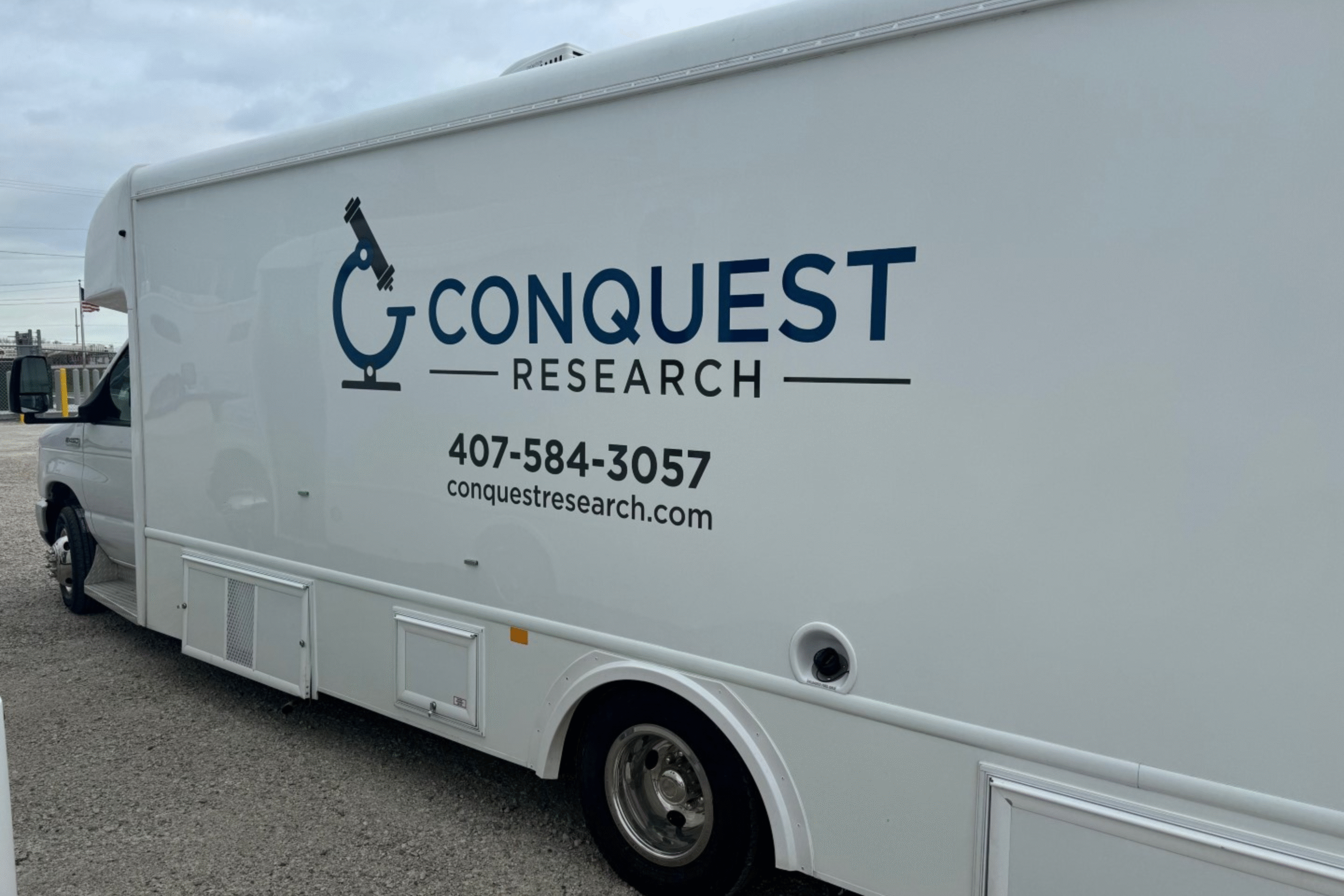 Photo of a white bus with Conquest Research logo and phone number