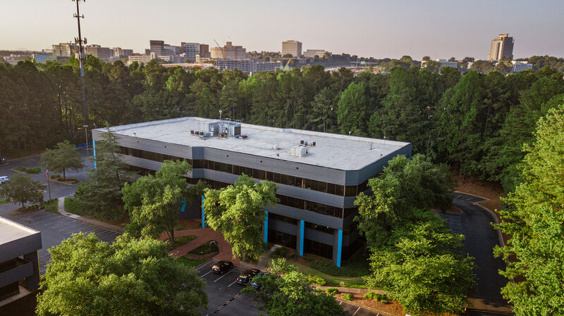 Aerial view of a modern, two-story clinical research facility surrounded by trees, with the Atlanta skyline visible in the background.
